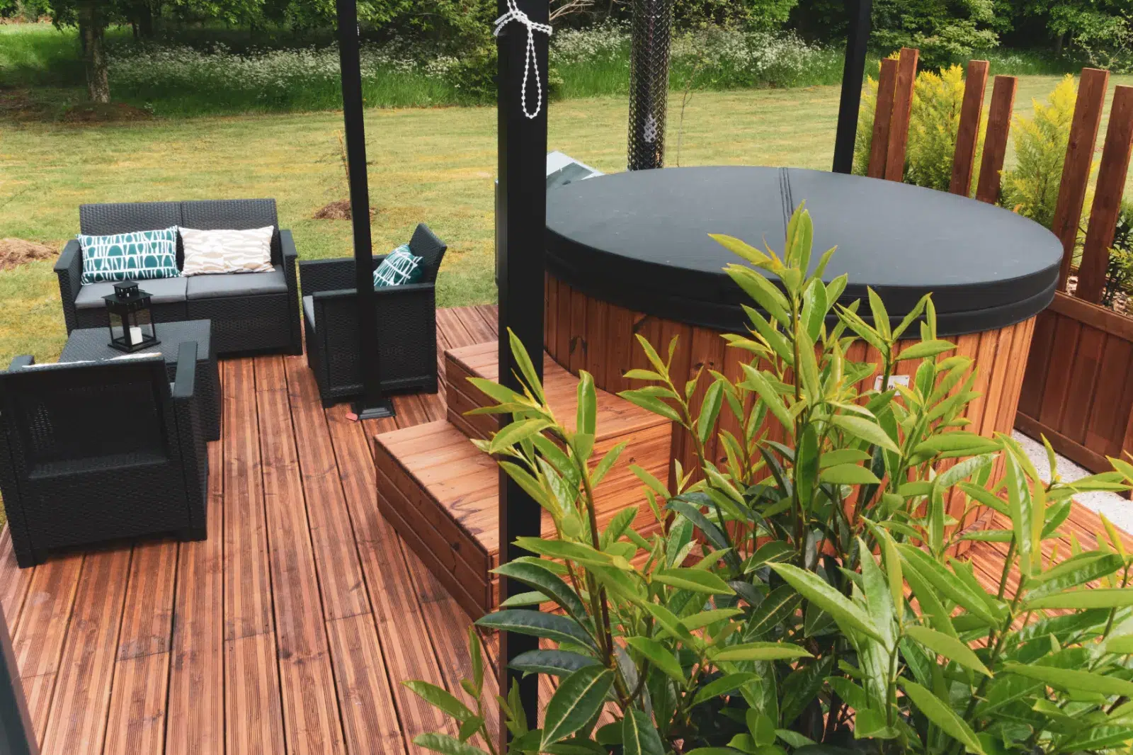 Jacuzzi extérieur en bois sur terrasse avec pergola, dans un jardin verdoyant