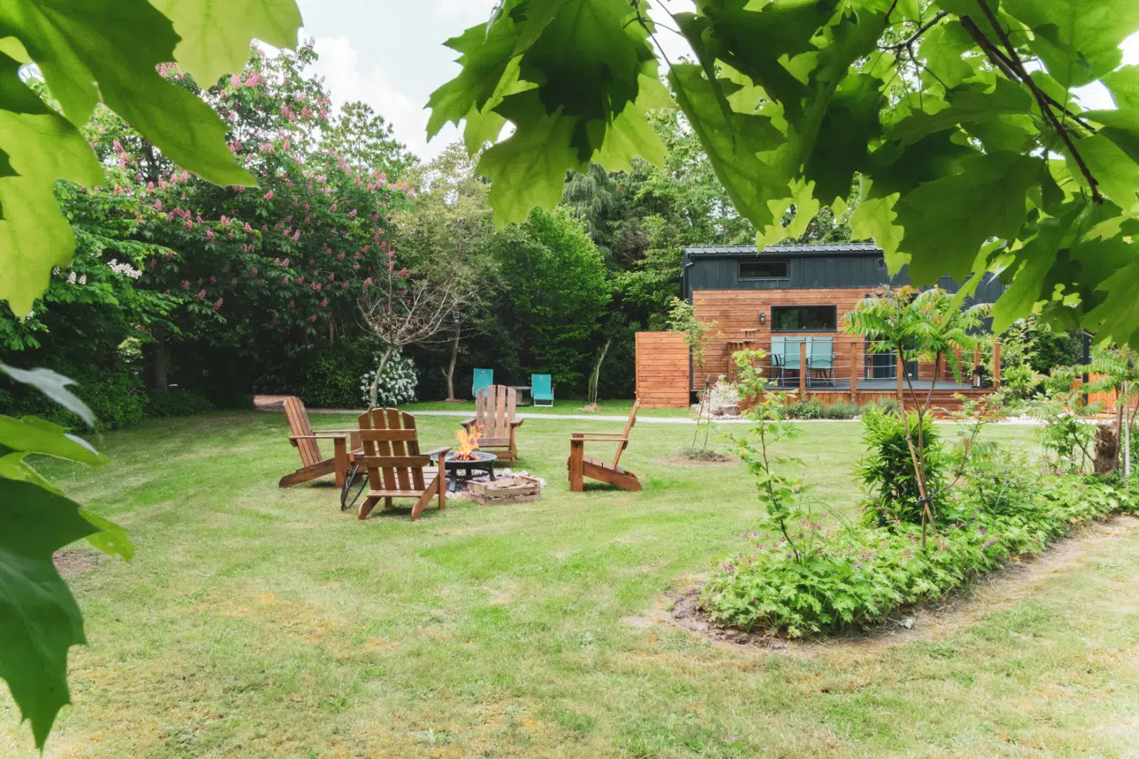 Jardin arboré avec brasero et chaises en bois devant un gîte moderne
